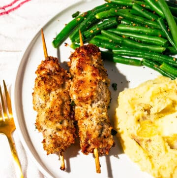 City chicken skewers with green beans and mashed potatoes with a gold fork on the side.