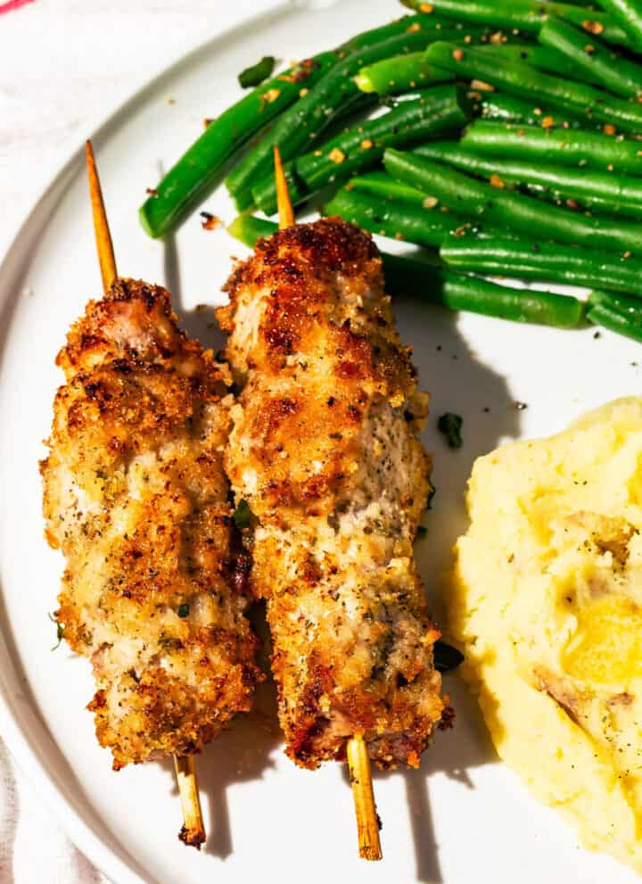 City chicken skewers with green beans and mashed potatoes with a gold fork on the side.