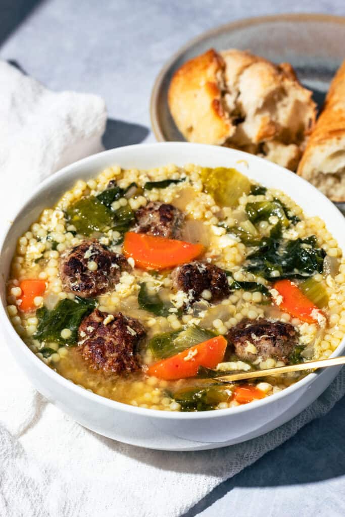 A bowl of Italian wedding soup with a gold spoon.