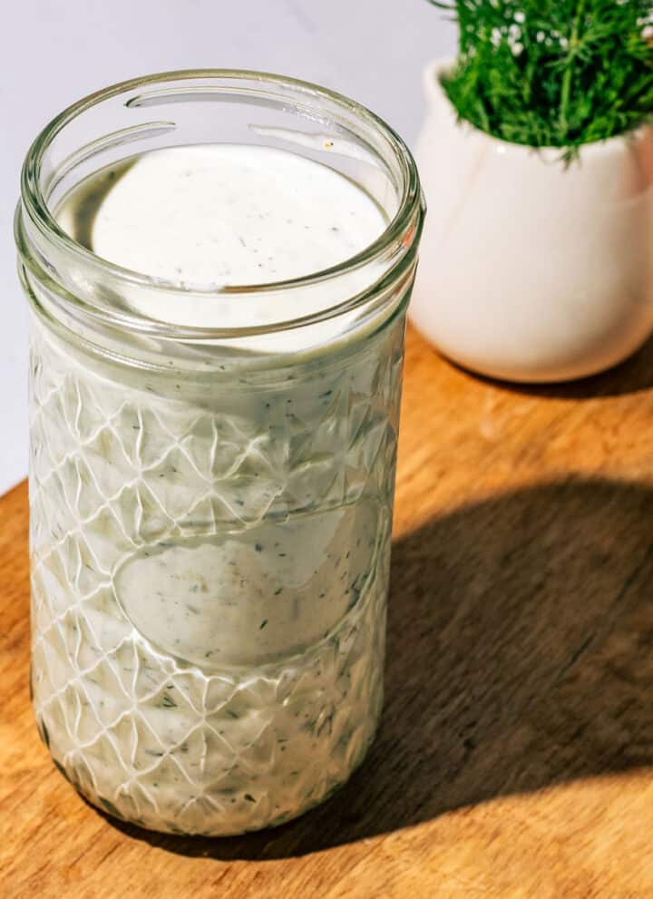 Jar of the dill ranch dressing with fresh dill in the background.