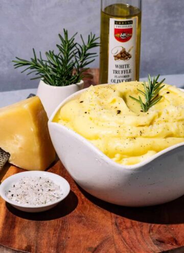 A bowl of mashed potatoes on a wood surface with a bottle of truffle oil in the background.