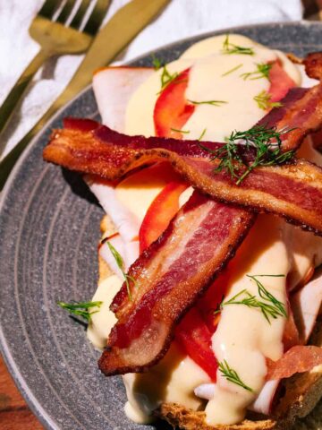 The turkey devonshire on a gray plate with bacon on top.