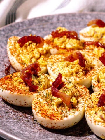 Deviled eggs garnished with crumbled candied bacon, paprika, and dill.