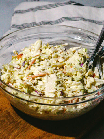 Bowl of coleslaw on a wood surface with a blue and white napkin on the side.